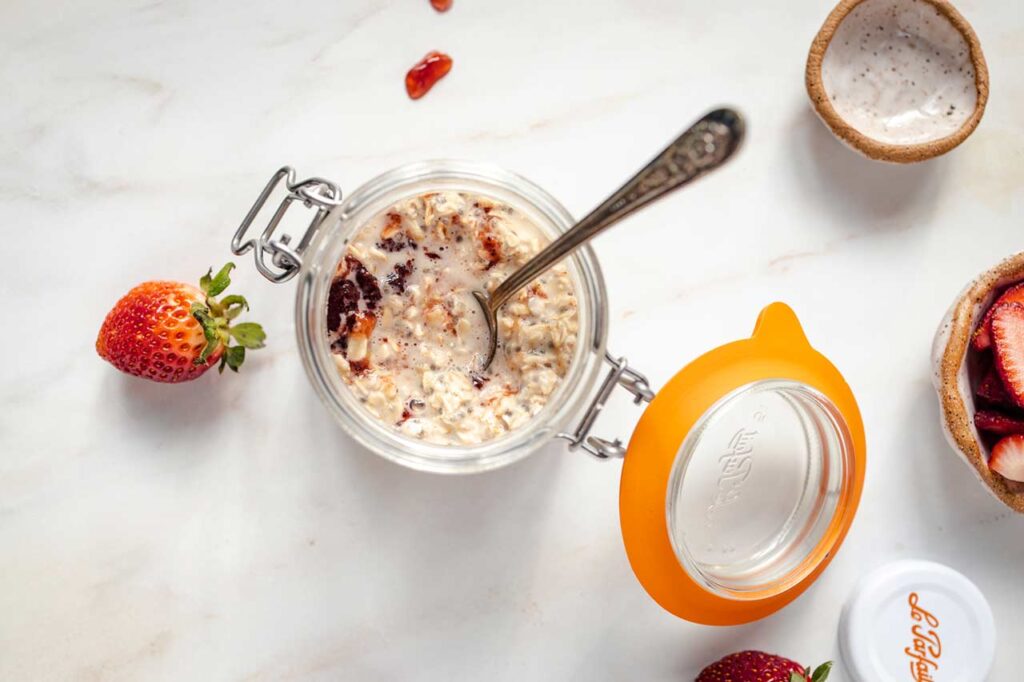 Fruit spread stirred into overnight oats in an open canning jar with a spoon resting in it.