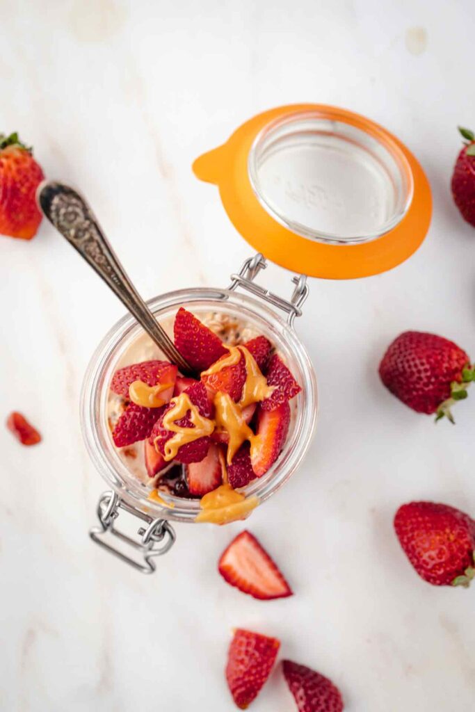 An overhead view of an open canning jar filled with Peanut Butter and Jelly Overnight Oats with a spoon resting in it.