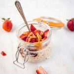 A side view of an open canning jar filled with Peanut Butter and Jelly Overnight Oats with a spoon resting in it.