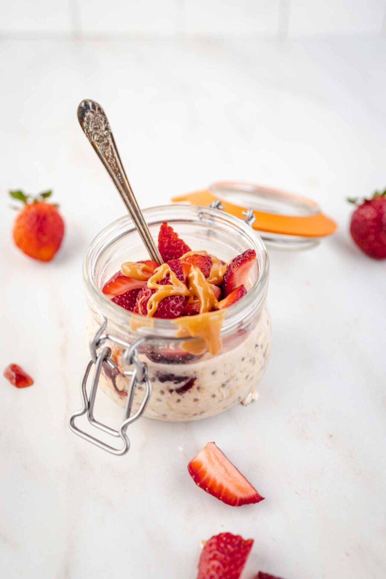 A side view of an open canning jar filled with Peanut Butter and Jelly Overnight Oats with a spoon resting in it.