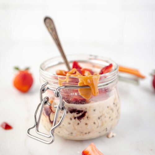 A front view of an open canning jar filled with Peanut Butter and Jelly Overnight Oats with a spoon resting in it.