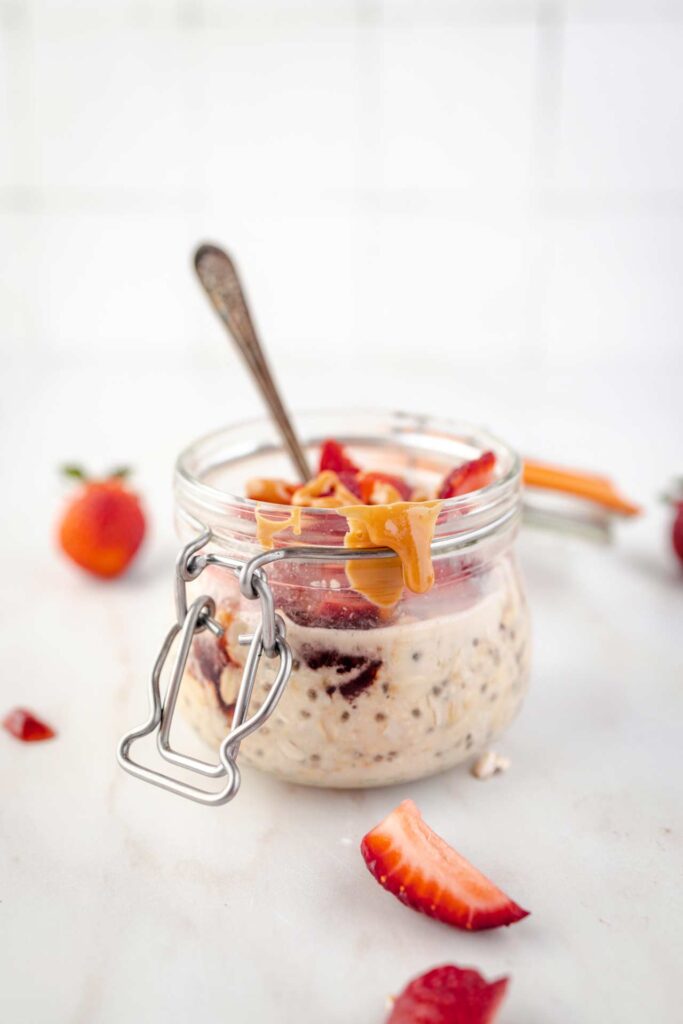 A front view of an open canning jar filled with Peanut Butter and Jelly Overnight Oats with a spoon resting in it.