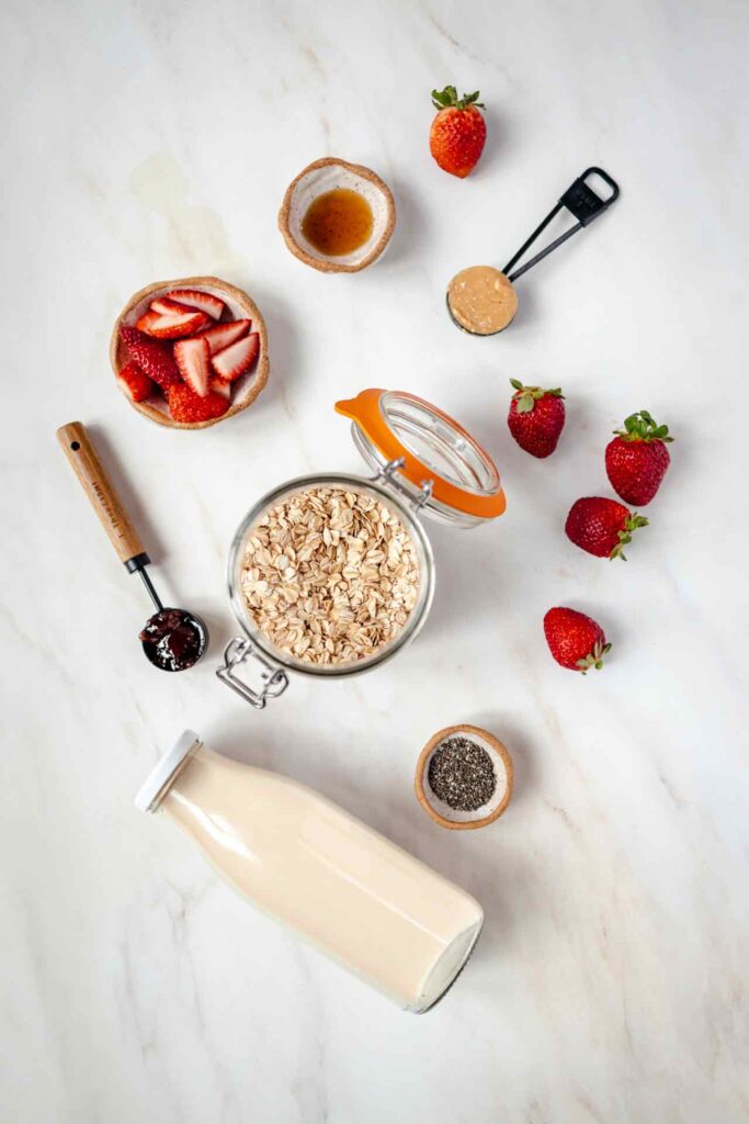 An overhead view of all Peanut Butter and Jelly Overnight Oats recipe ingredients on a white surface.