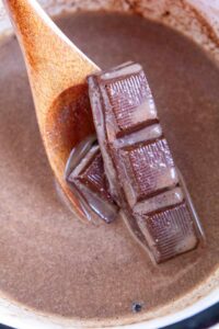 A wooden spoon stirs chocolate pieces in milk with sweetener.