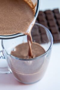 Pouring hot chocolate into a glass mug.