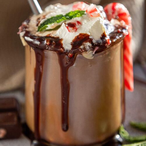 A side view of a glass mug filled with peppermint hot chocolate topped with whipped cream and chocolate sauce.