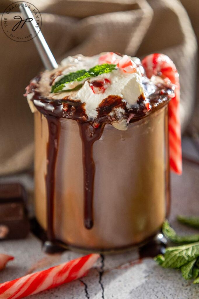 A side view of a glass mug filled with peppermint hot chocolate topped with whipped cream and chocolate sauce.