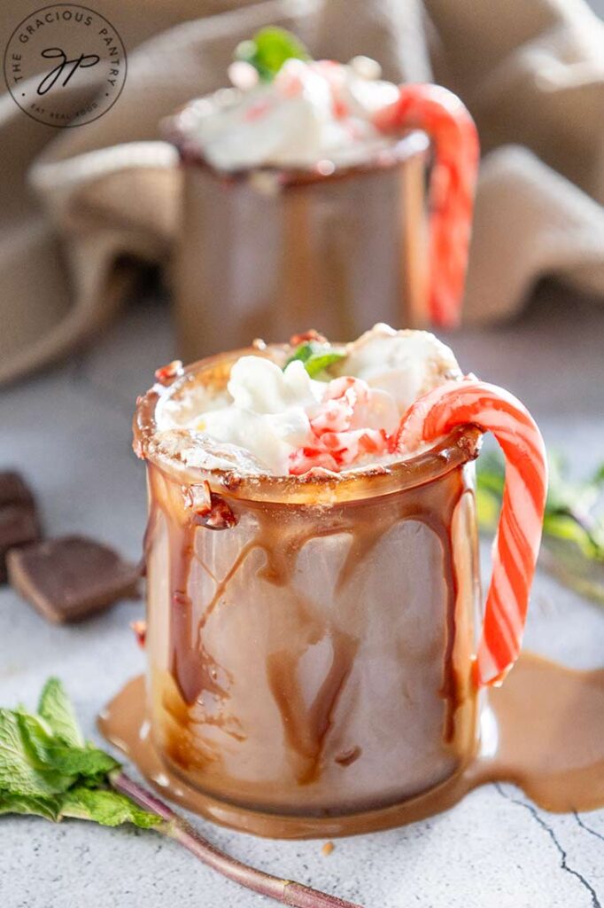 A side view of two mugs filled with peppermint hot chocolate. Candy canes hang off the edge of the mug.