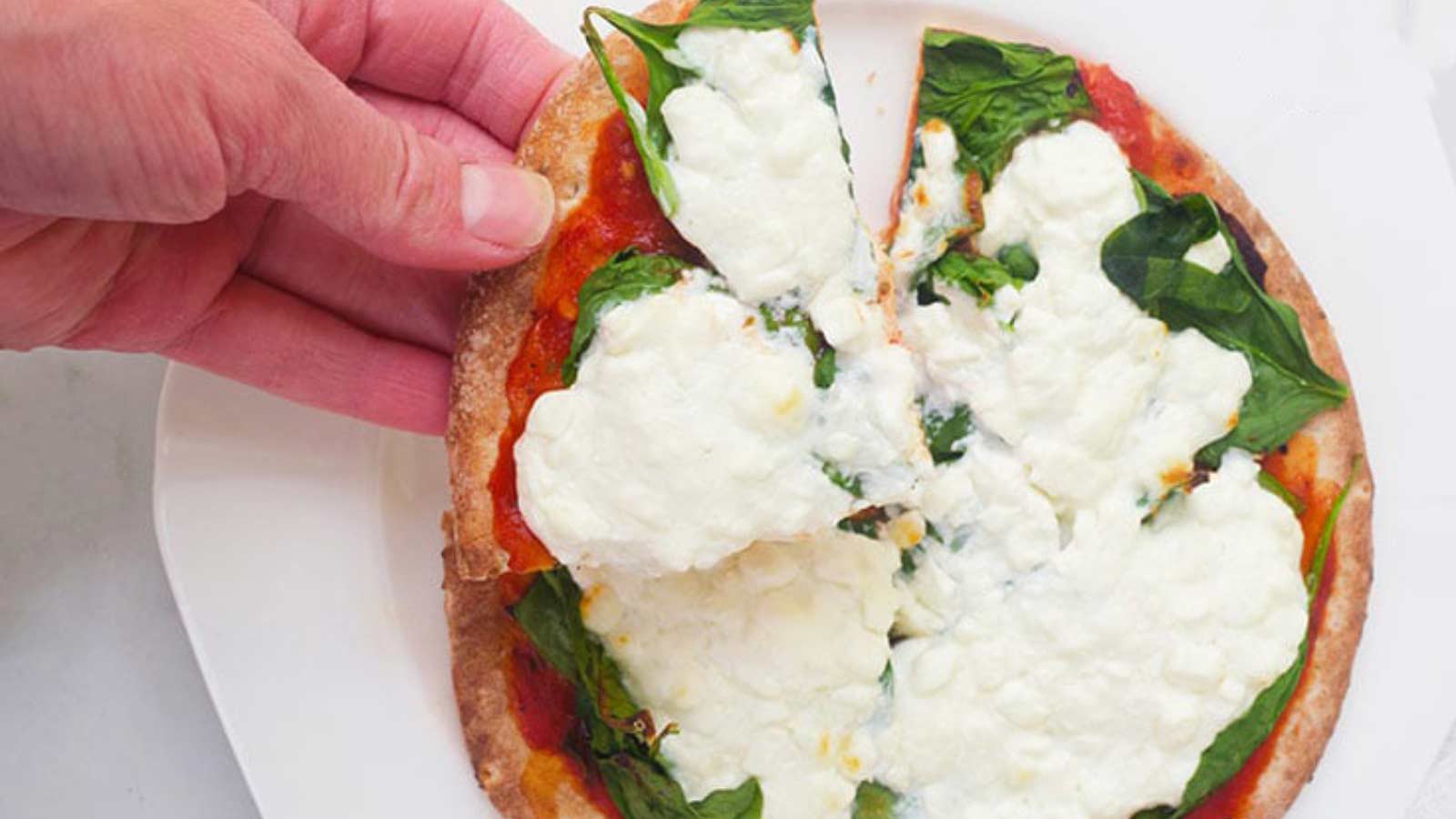 A hand reaches for a slice of Pita Pizza from a white plate.
