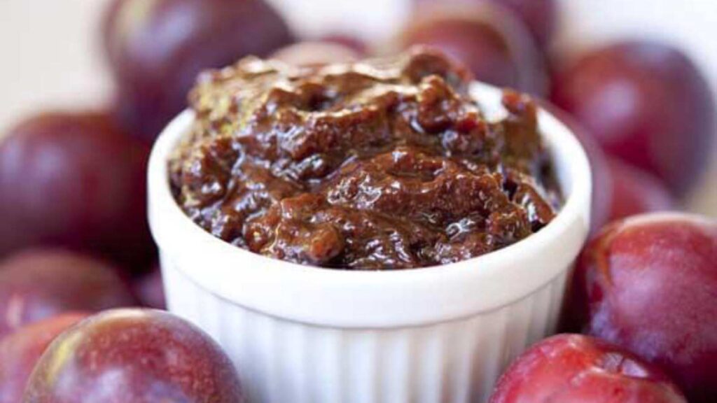Plum Butter in a white bowl surrounded by fresh plums.