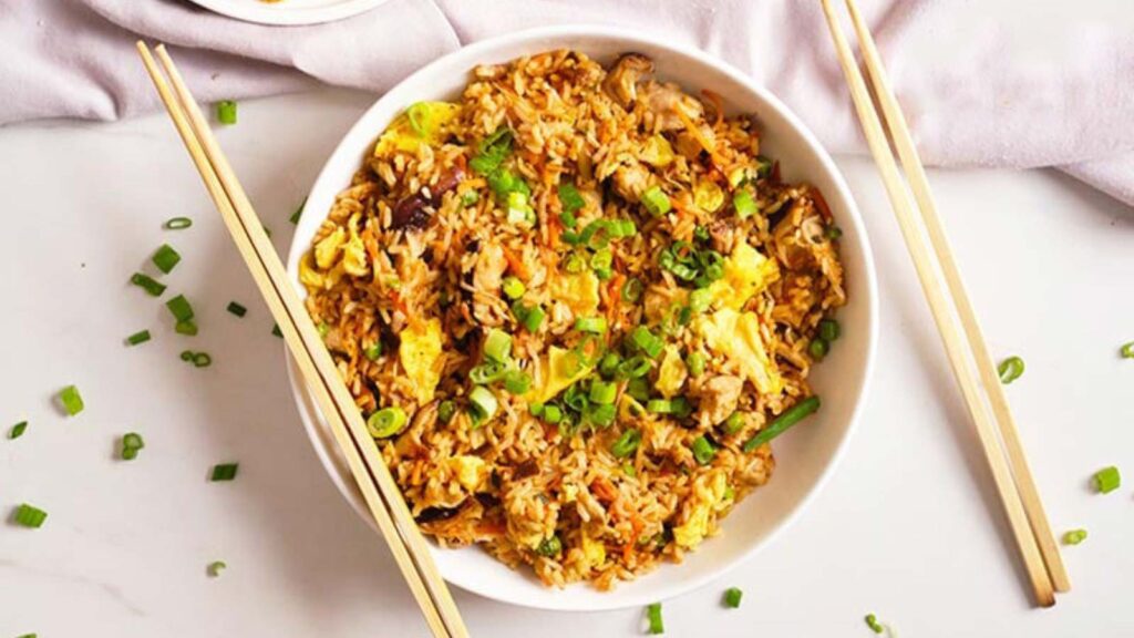 The finished Healthy Pork Fried Rice served in a white bowl with some chop sticks resting on the side of the bowl.