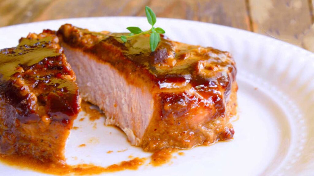 A single pork chop on a white plate with pork marinade covering it. It has been sliced open.