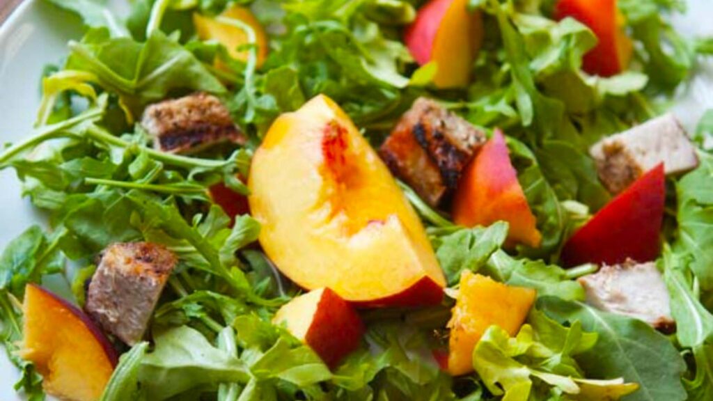 A closeup of a peach pork salad on a white plate.