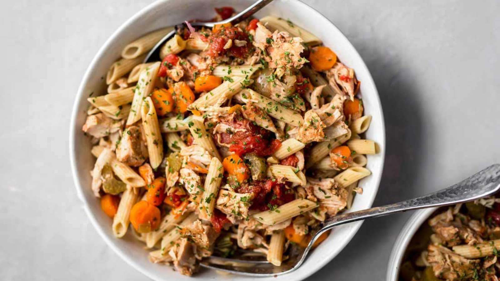 A white bowl filled with pork ragout. Serving spoons lay in the bowl.