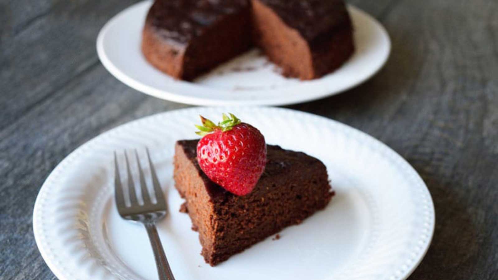 A slice of Instant Pot Chocolate Cake sits on a white plate with a fork resting at it's side.