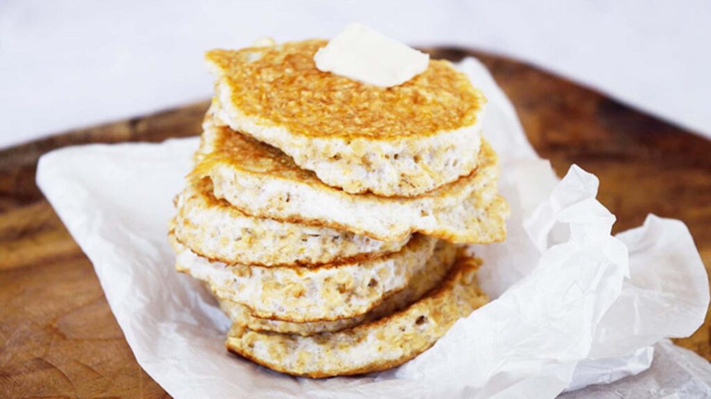 A stack of protein pancakes sitting on a piece of parchment paper with a pat of butter on top of the stack.