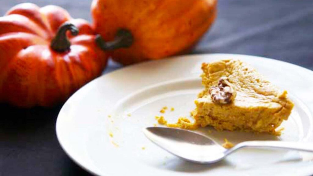 A piece of Pumpkin Cheesecake, partially eaten, on a white plate with a spoon.