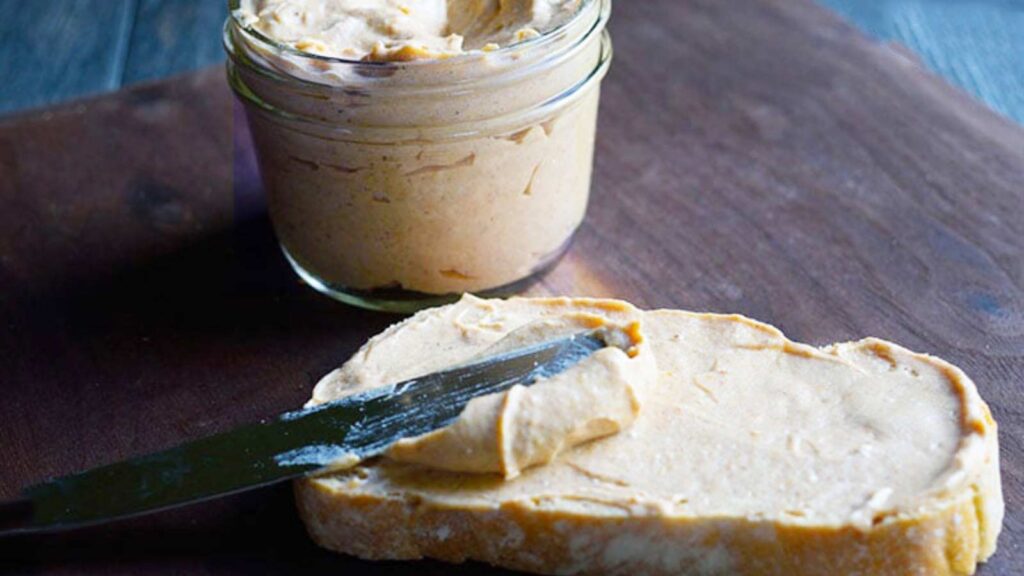 A knife spreads some pumpkin cream cheese over a slice of bread.