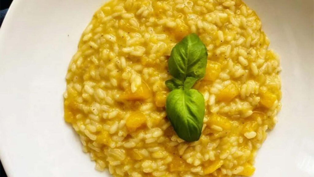 Creamy Pumpkin Risotto in a white bowl, garnished with two fresh basil leaves.