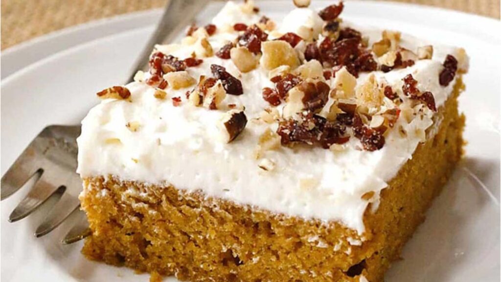 A closeup of a slice of Pumpkin Sheet Cake with White Chocolate Cream Cheese Frosting on a white plate with a fork.