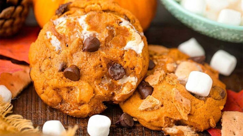 Closeup of Pumpkin S’mores Cookies on a table with mini marshmallows around them.