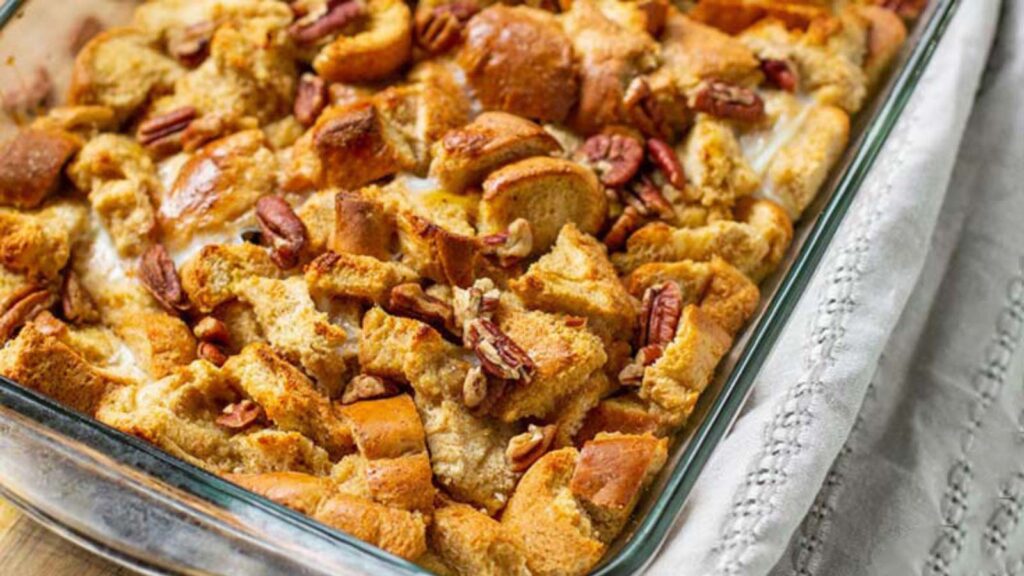 A casserole dish filled with Pumpkin Spice French Toast Casserole, sitting on a table with a towel.