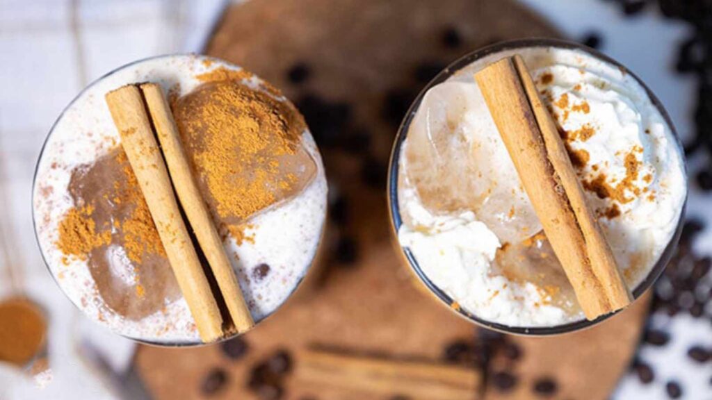 An overhead view of two glasses filled with pumpkin spice latte and topped with cinnamon sticks.