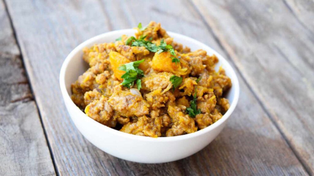 A white bowl filled with Pumpkin Turkey, sitting on a wood surface.
