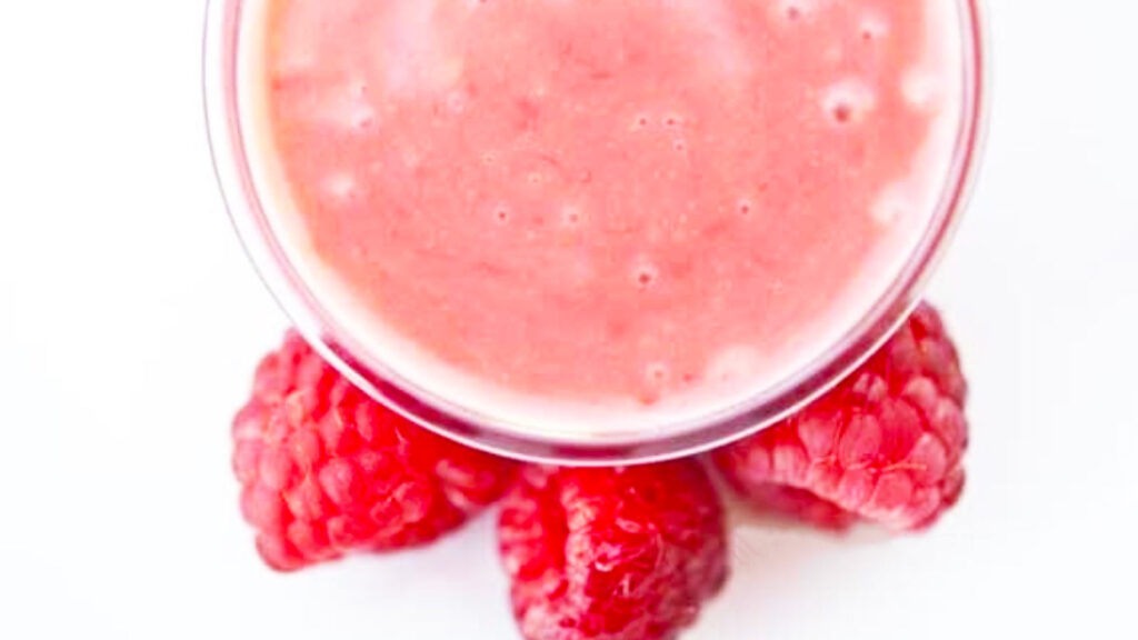 An overhead view of a jar of Raspberry Vinaigrette with three fresh raspberries next to the jar.