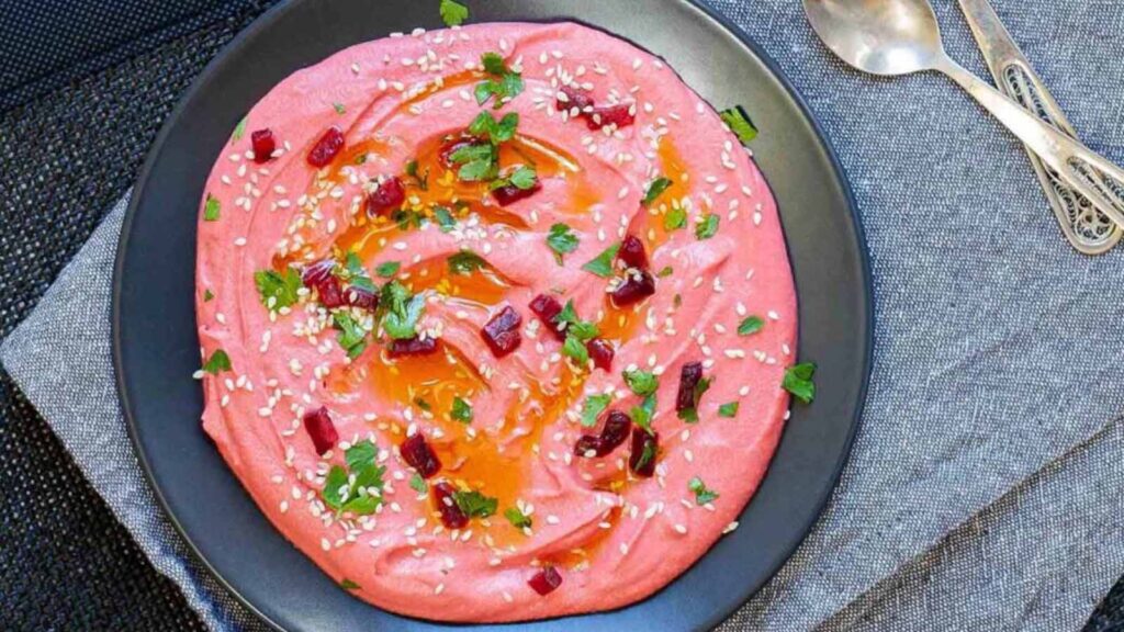 A black bowl filled with pink roasted beet hummus.