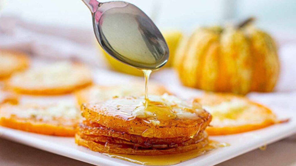 A spoon drizzles some syrup over slices of squash on a platter.