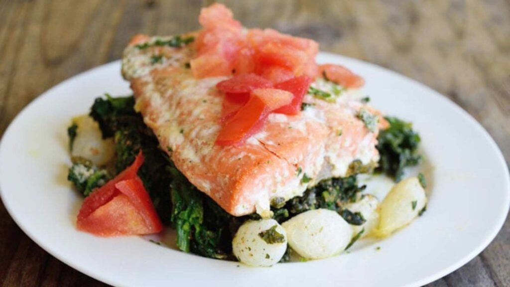 A salmon filet on a bed of spinach topped with chopped tomatoes.