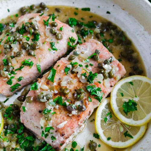 Two salmon filets in a skillet with herbs, oil an lemon slices.