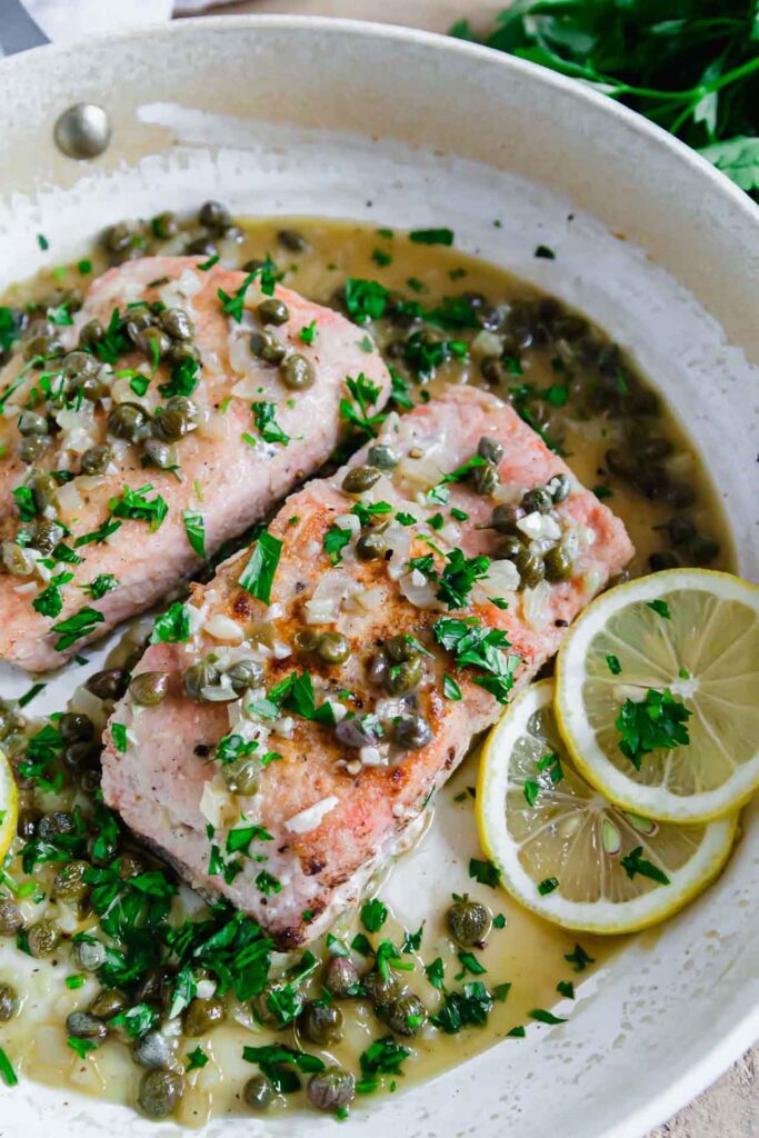 Two salmon filets in a skillet with herbs, oil an lemon slices.