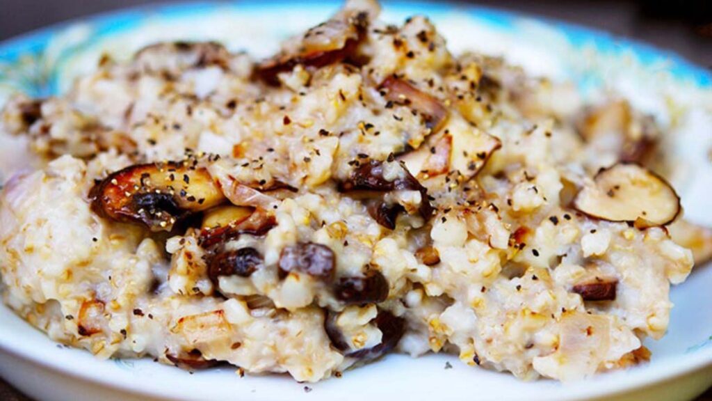 A bowl of Savory Oatmeal sits on a dark background. You can see the golden color of the sautéed mushrooms mixed into the oats.