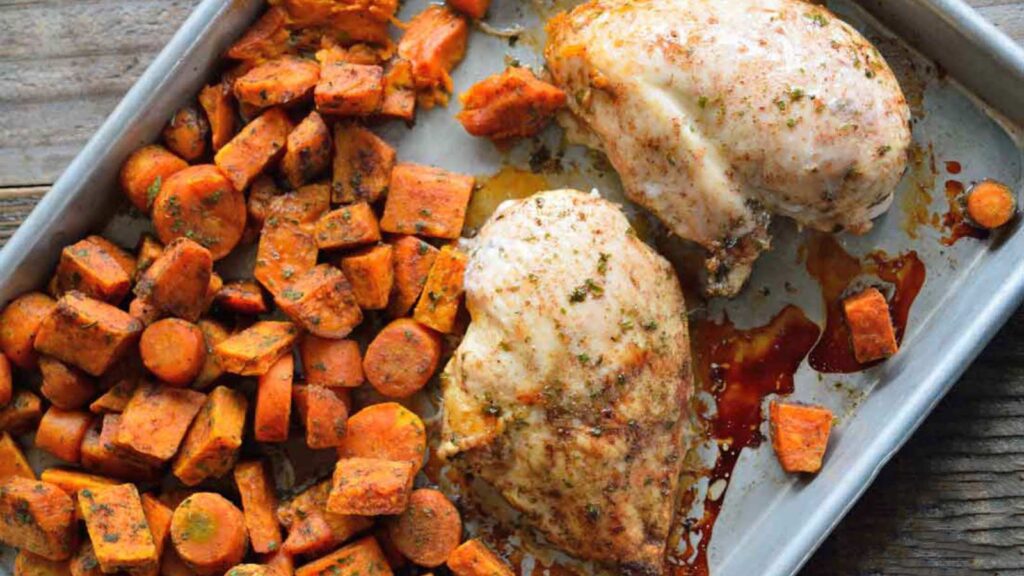 A sheet pan from overhead filled with carrots and two chicken breasts.
