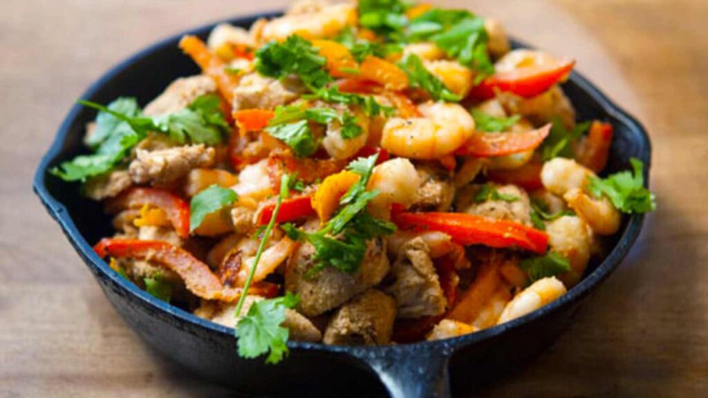 Barbecued Southwestern Chicken And Shrimp Skillet in a cast iron skillet on a wood surface.