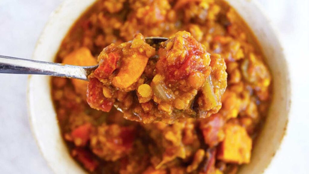 A spoon lifts a spoonful of Slow Cooker Lentil Stew out of a bowl.