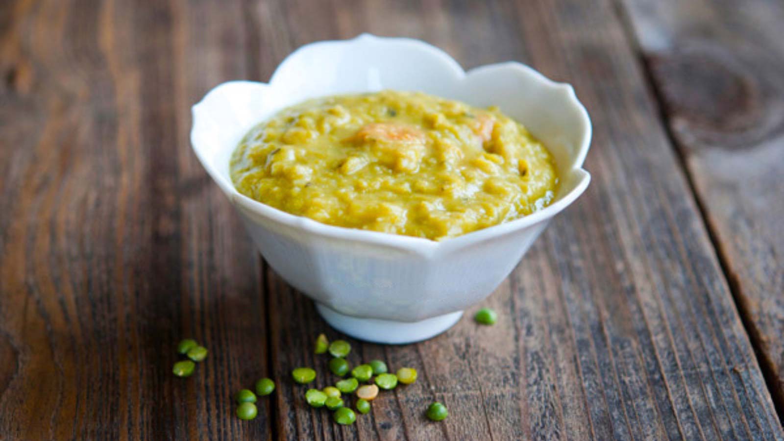 A white bowl filled with Split Pea Soup on a wood surface.