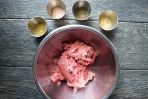 Ground turkey in a mixing bowl. Spices in small containers sit around the bowl.