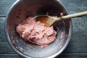 Ground turkey mixed with seasoning in a mixing bowl with a wooden spoon.