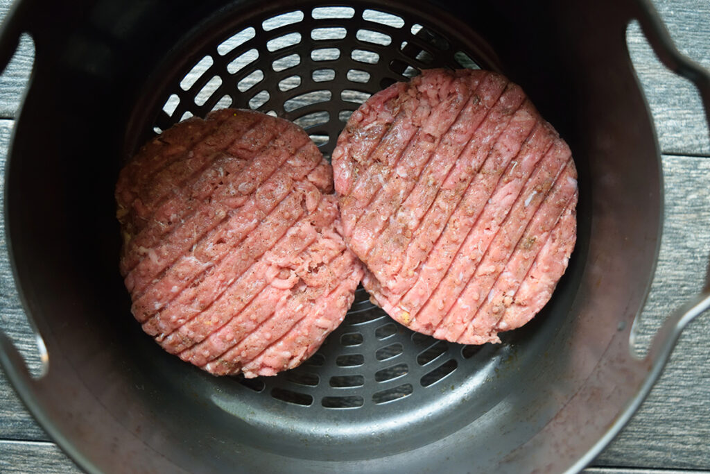 Two raw turkey patties sitting in an air fryer basket.