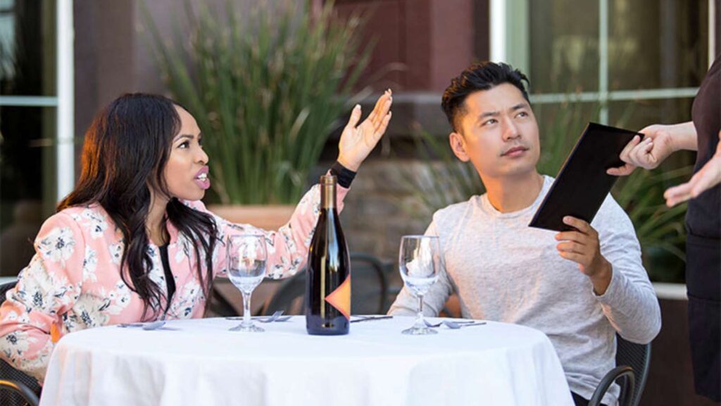 A couple complaining to a waitress at a cafe table.