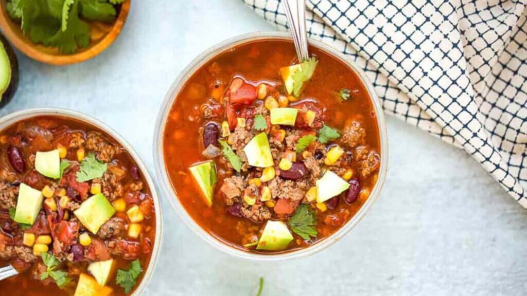 An overhead view of two bowls of taco soup garnished with avocado and fresh cilantro.