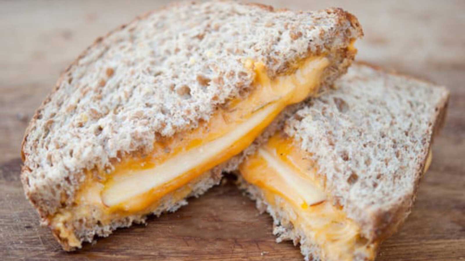 A closeup of a cut Fire Pit Thyme And Apple Grilled Cheese Sandwich laying on a cutting board.