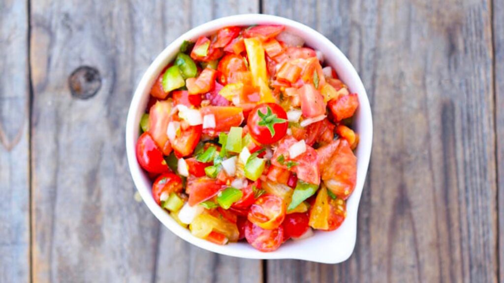 An overhead view of a white bowl filled with Marinated Tomato Salad.