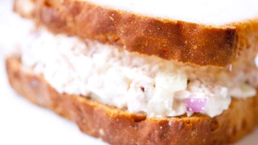 A close up of a tuna fish sandwich on a white background.