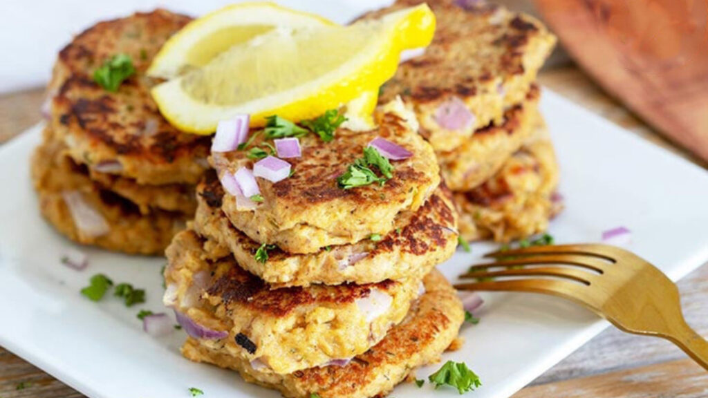 Freshly cooked, clean eating tuna patties sit on a plate with a lemon wedge, ready to eat.