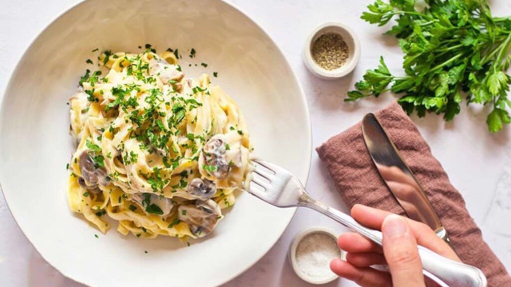 A hand holds a fork and reaches for a fork full of Vegan Fettuccine Alfredo