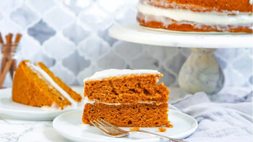 A slice of Vegan Pumpkin Spice Cake With Cream Cheese Frosting sitting on a white plate with a fork.